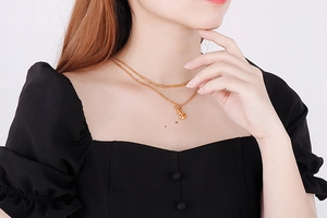 Detail of a double-layered gold necklace with a saxophone pendant on a paperclip chain