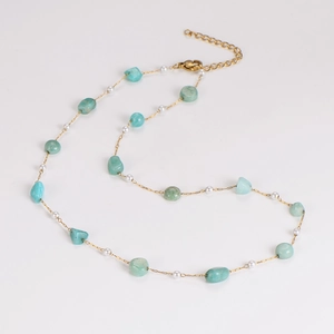 Detailed macro view of a gold chain necklace with green stones and small white pearls