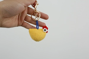 Close-up of a handmade yellow crochet chicken keychain with golden metal ring detail