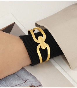 Detailed view of a gold-plated interlocking geometric cuff on a model's wrist