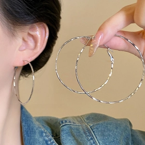Close-up of silver twist hoop earrings showing large circular design worn on ear
