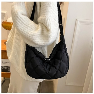 Detail of black quilted hobo bag with adjustable strap worn by model in a minimal setting