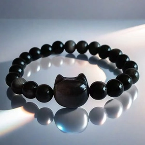 Macro detail of obsidian black bead bracelet featuring a central cat head charm with reflection