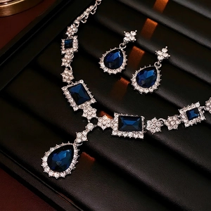 Elegant jewelry set with blue square and teardrop crystal pendants on black display