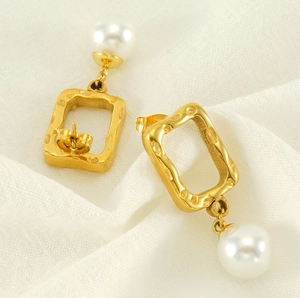 Close-up of golden hammered rectangle earrings with white pearls on white fabric