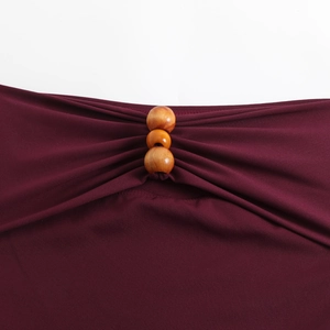 Close-up of wine red swimsuit fabric featuring bohemian wooden beads and pleated details