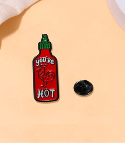 Detail of red hot sauce bottle enamel pin with You're Hot text and rooster design