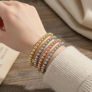 Detail of four stackable 18K gold-plated beaded elastic bracelets on a female wrist