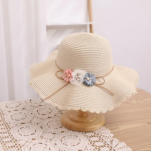 Détail d'un chapeau de paille beige avec bord festonné et fleurs en tissu 3D élégantes