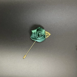 Close-up of handmade emerald green satin rose lapel pin with golden leaf and long metal needle
