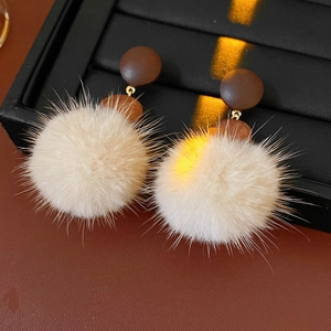 Macro shot of fluffy cream pom pom earrings with dark brown studs on a black display
