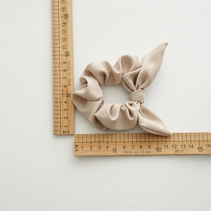 Close-up of beige bow hair tie showing high elasticity and soft satin fabric texture