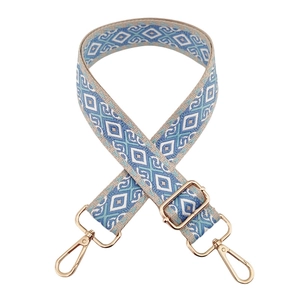 Close-up of beige woven bag strap with blue diamond pattern and gold metal buckles