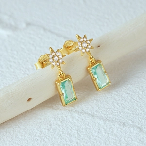 Detail of S925 silver star earrings with emerald green stones on wooden display
