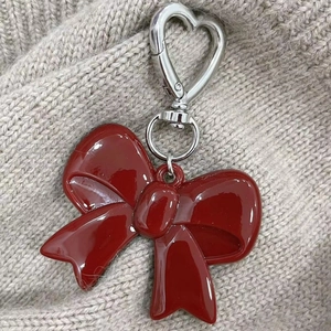 Macro detail of red acrylic bow pendant with silver heart-shaped lobster clasp on knit fabric