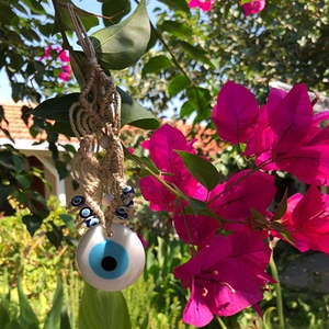 Turkish Blue Evil Eye glass pendant with rope hanger displayed in garden flowers