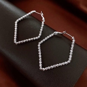 Detailed close-up of silver rhombic geometric hoop earrings with textured spiral wire design