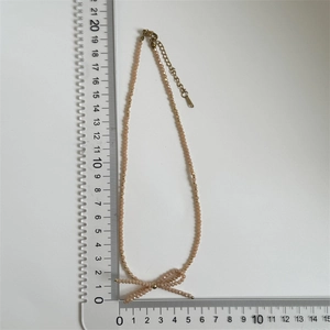 Detail view of a handmade beaded bow necklace with faceted crystal beads and scale ruler