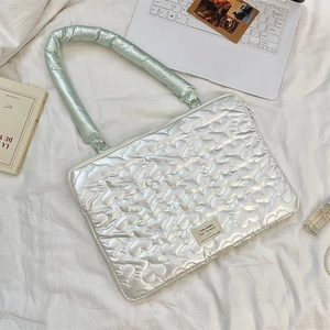 Detail of silver heart-quilted laptop bag with soft green handle and metal zipper