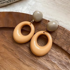 Detail of retro oval resin drop earrings in khaki and taupe on a wooden display tray