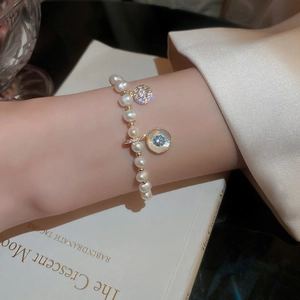 Detail of a pearl bracelet with gold floral charms and crystals on a female wrist