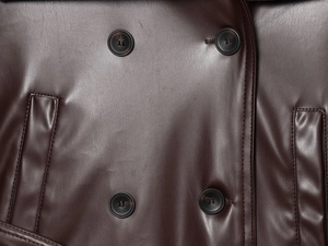 Detailed macro view of the double-breasted buttons and pockets on the dark brown faux leather coat