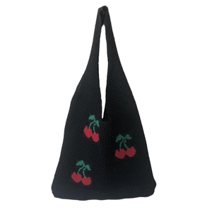 Detailed view of a black knitted tote bag featuring a vibrant red cherry pattern