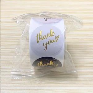 Macro shot of 1-inch marble thank you labels with gold foil text on a wooden surface