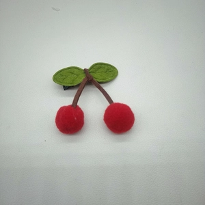 Detailed view of cute cherry hair clip with red pom-poms and green textured leaves