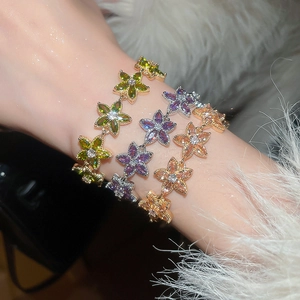 Close-up of stacked zircon flower bracelets in pink, green, and violet on a model's wrist
