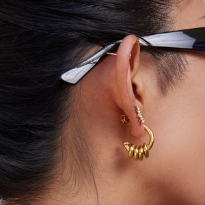Close-up of a model wearing a two-tone multi-layered C-shaped earring and a sparkling ear cuff