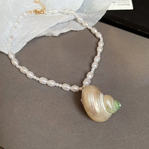 Detailed close-up of baroque pearl necklace with natural conch shell pendant and gold clasp