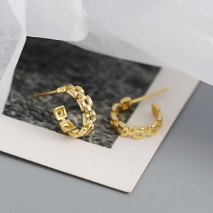 Macro shot of gold chain link C-shaped earrings on a minimalist photography card