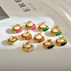 Macro view of geometric gold earrings featuring colorful enamel inlay on white fabric