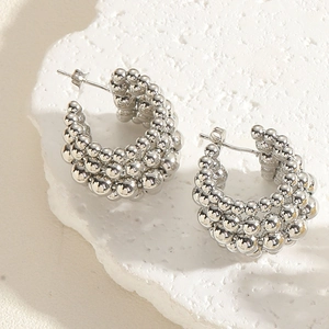 Close-up of silver C-shaped bead earrings on a textured stone tray with side lighting