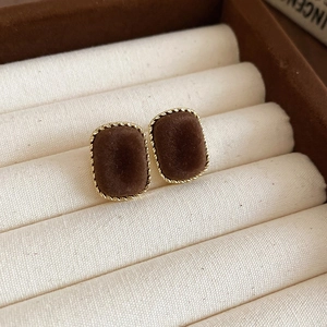 Detail of square brown velvet stud earrings with golden braided texture in jewelry box