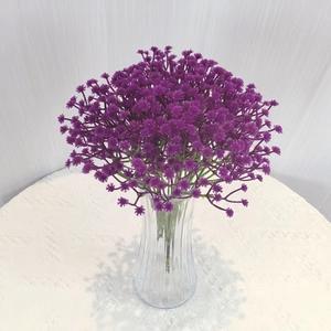 Deep purple gypsophila artificial flowers in a fluted glass vase on white lace cloth