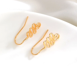 Close-up of golden wavy wire earrings on a white ceramic plate and silk fabric