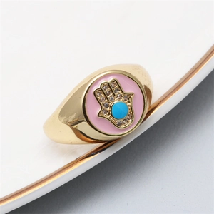 Macro detail of golden Hamsa Hand ring with pink enamel and blue center stone
