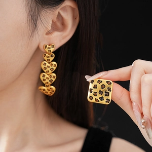 Detailed view of leopard print heart drop earrings and square stud on gold metal