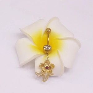 Piercing de nombril fleur dorée avec cristaux roses posé sur une fleur de frangipanier