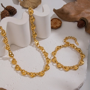 Golden stainless steel heart-link necklace and bracelet set on white stone with autumn decor