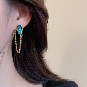Close-up of elegant gold chain drop earrings with emerald green rectangular gemstones