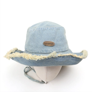Detail of light blue denim bucket hat with frayed edges and metal logo plate with chin cord