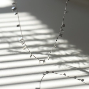 Minimalist silver bead chain necklace with rectangle pendants on a light and shadow background