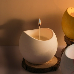 Primo piano di una candela profumata accesa in un vasetto di ceramica bianca opaca