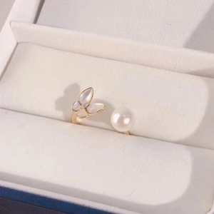 Elegant gold ring featuring a white butterfly shell and round pearl on a jewelry display
