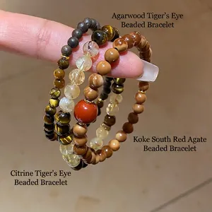 Three beaded bracelets with citrine and tiger eye stone held by hand on beige tile