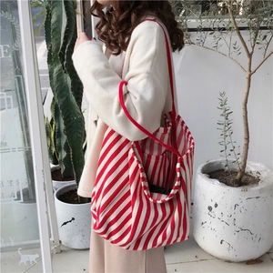 Side view of large red and white striped canvas tote bag worn by a model in outdoor setting