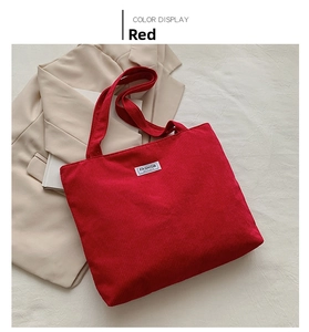 Close-up of red corduroy tote bag with FASHION patch on white textured background